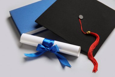 Mavi kurdeleli diploma, mezuniyet şapkası ve beyaz arka plan kitabı.