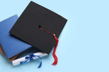 Kurdeleli diploma, mezuniyet şapkası ve mavi arka plan kitapları.