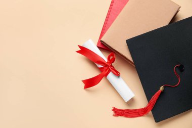 Kırmızı kurdeleli diploma, mezuniyet şapkası ve bej arka plan kitapları.