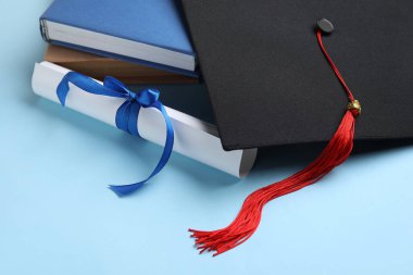 Kurdeleli diploma, mezuniyet şapkası ve mavi arka plan kitapları.