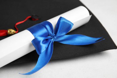 Diploması mavi kurdeleli ve mezuniyet şapkası beyaz masada.