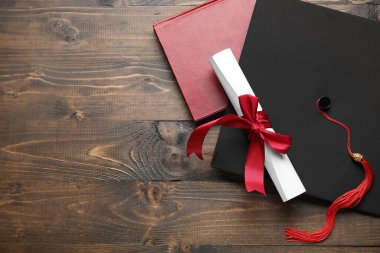 Kırmızı kurdeleli diploma, mezuniyet şapkası ve ahşap masa üzerine kitap.