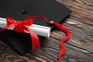 Diploması kırmızı kurdele ve ahşap masada mezuniyet şapkası.
