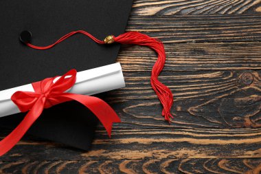 Diploması kırmızı kurdele ve ahşap masada mezuniyet şapkası.