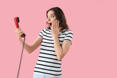 Pembe arka planda telefon ahizesiyle şok olmuş genç bir kadın.