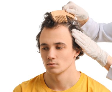 Doktor beyaz arka planda genç adamın saçını tarıyor.