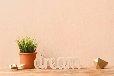 Bej duvarın yanındaki masada dekoru olan yapay çimenler.