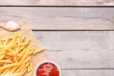 Ahşap arka planda lezzetli patates kızartması, tuz ve ketçap.
