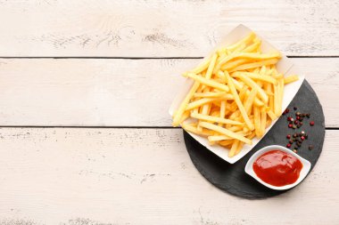 Lezzetli patates kızartması, ketçap ve ahşap arka planda biber içeren karton kutu.