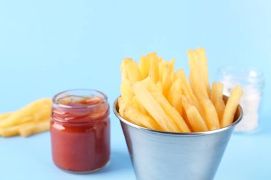 Lezzetli patates kızartması, ketçap ve açık mavi arka planda tuz içeren metal bardak.