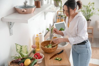 Genç bir kadın mutfakta sebze salatası yapıyor.