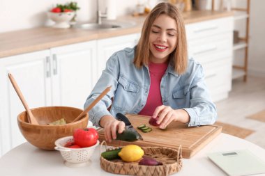Genç bir kadın mutfakta sebze salatası yapıyor.
