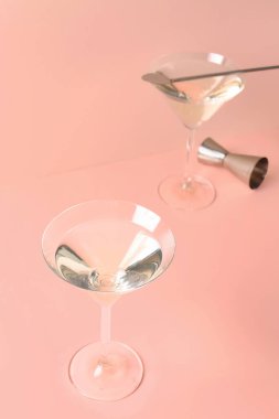 Bir bardak martini, bar kaşığı ve pembe arka planda jigger.