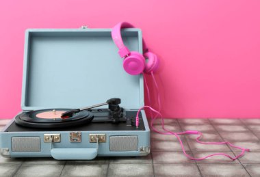 Pembe duvarın yanındaki masada vinil diski ve kulaklığı olan kayıt çalar
