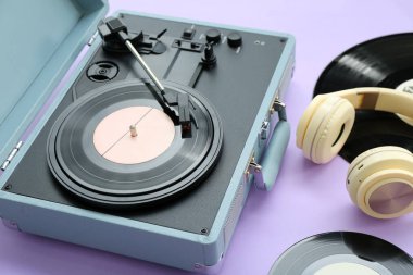 Eflatun arka planda vinil diskleri ve kulaklıkları olan kayıt çalar