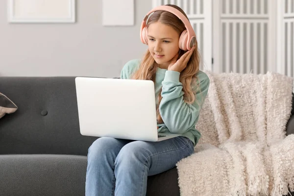 stock image Little girl in headphones using laptop on sofa at home