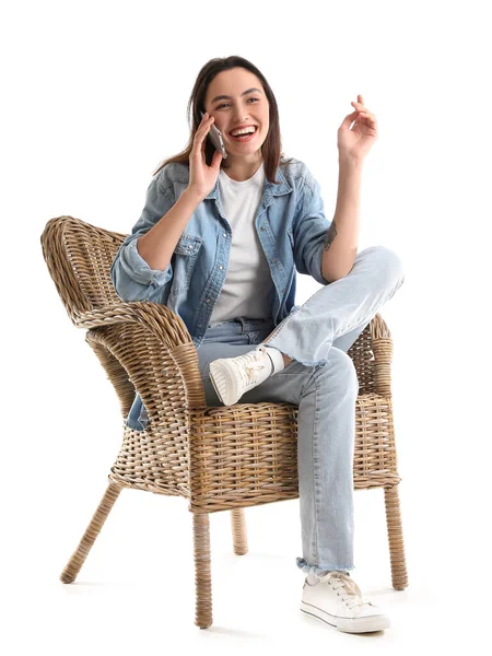 年轻女子坐在白色背景的柳条扶手椅上 用手机交谈 — 图库照片