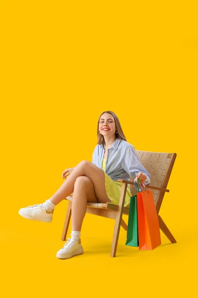 Młoda Kobieta Torbami Zakupy Siedzi Drewnianym Fotelu Żółtym Tle — Zdjęcie stockowe