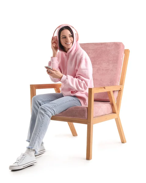 美しいです女性とともにヘッドフォンと携帯電話に座ってピンクアームチェア上の白い背景 — ストック写真