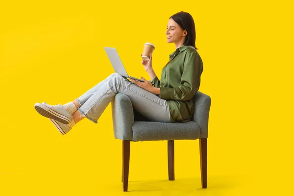 노란색 배경에 부드러운 안락의자에 랩탑을 사용하여 커피를 마시고 아름다운 — 스톡 사진