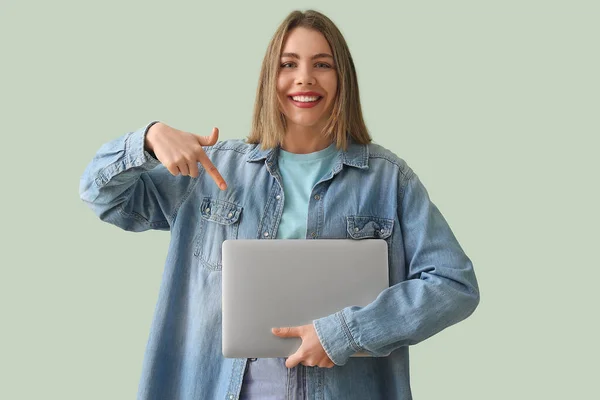 Young woman in denim shirt with laptop on green background