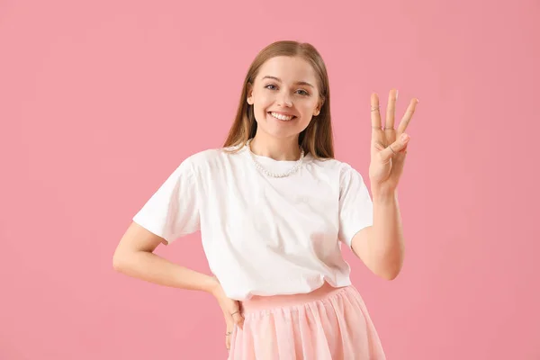 ピンクの背景に3本の指を示すTシャツの若い女性 — ストック写真