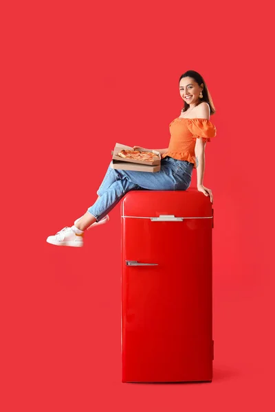 Schöne Frau Mit Leckerer Pizza Sitzt Auf Kühlschrank Vor Rotem — Stockfoto