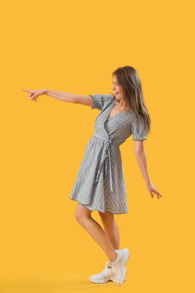 Sarı Arka Plandaki Bir Şeyi Gösteren Çizgili Elbiseli Güzel Kadın — Stok fotoğraf