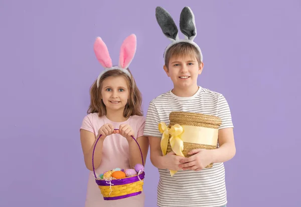 ライラックを背景にイースターエッグのバスケットを持つウサギの耳の小さな子供たち — ストック写真