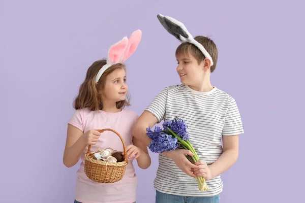 ライラックの背景にイースターエッグと花を持つウサギの耳の中の小さな子供 — ストック写真