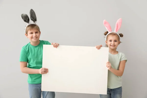 灰色の背景に空白のポスターを持つウサギの耳の小さな子供たち イースターのお祝い — ストック写真
