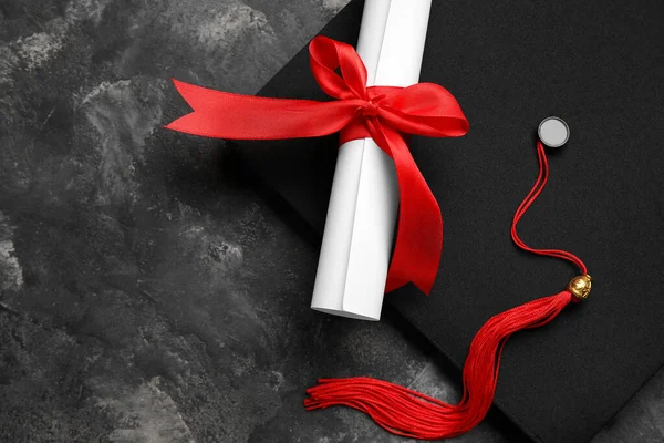 有红色缎带和深灰色桌子上的毕业帽的文凭 — 图库照片
