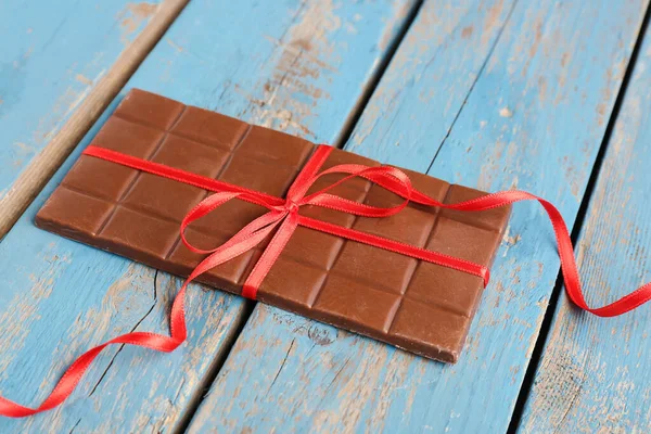 Stock image Tasty chocolate bar tied with red ribbon on color wooden background