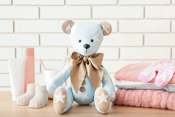 Speelgoedbeer Met Babykleertjes Accessoires Tafel Bij Witte Bakstenen Muur — Stockfoto