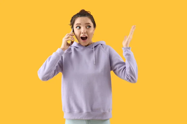 Sarı Arka Planda Akıllı Telefonlu Şok Olmuş Genç Bir Kadın — Stok fotoğraf