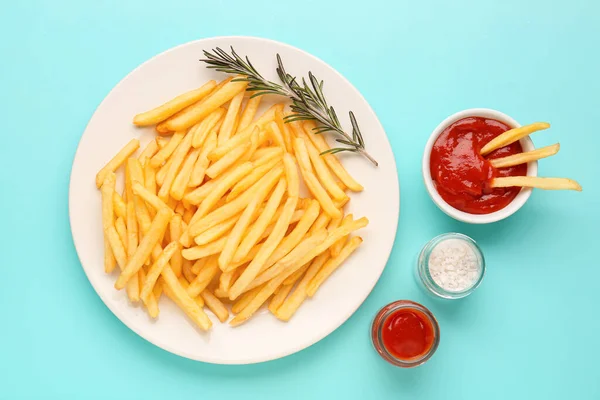 Plate with tasty french fries, ketchup and salt on light blue background