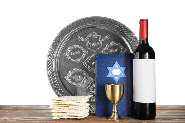 Bottle of wine, cup, Torah, Passover Seder plate and flatbread matza on wooden table against white background