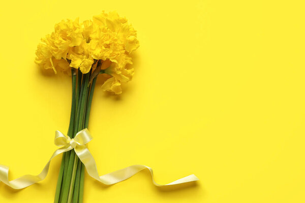 Beautiful narcissus flowers with yellow ribbon on color background