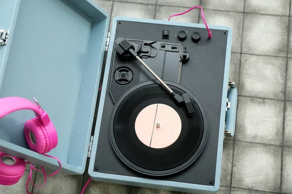Record player with vinyl disk and headphones on dark tile background