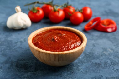 Lezzetli domates ezmesi, sarımsak ve taze sebzeli kase mavi grunge arkaplanda.