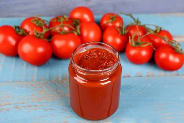 Mavi ahşap arka planda lezzetli domates ezmeli kavanoz.