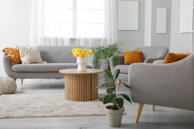 Oturma odasının içinde rahat bir kanepe, koltuklar ve sehpanın üzerinde vazo var.