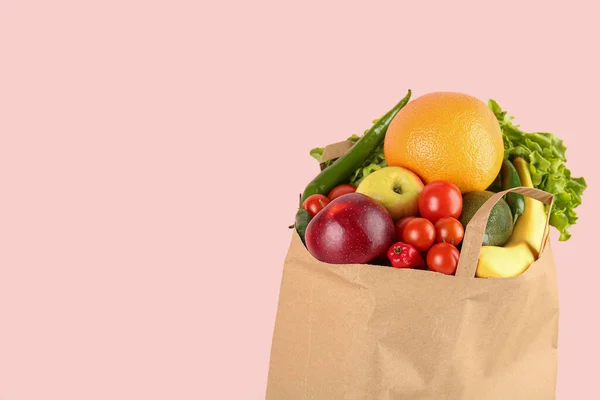 Paper bag with vegetables and fruits on pink background