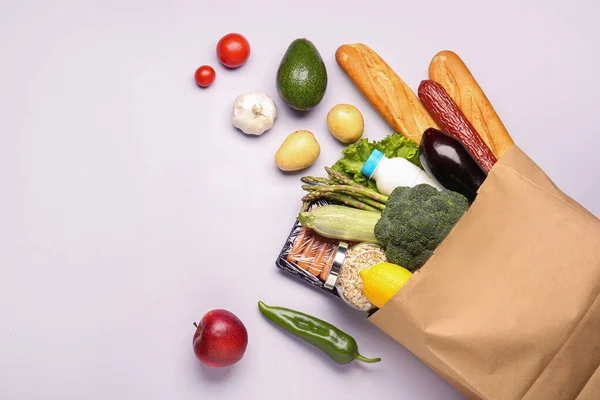 Paper bag with vegetables, cereal, bread and milk on grey background