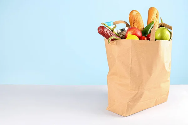 Paper bag with vegetables, fruits, sausage, bread and milk on table