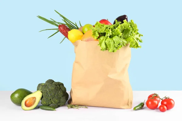 Paper bag with vegetables, fruits and sausage on table