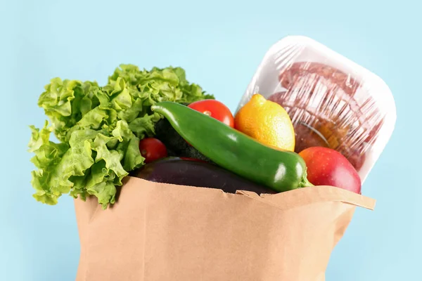Paper bag with vegetables, fruits and sausages on light blue background