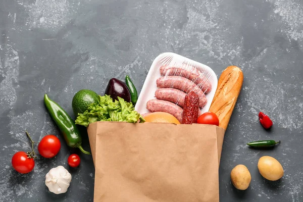 Paper bag with vegetables, sausages and bread on grey grunge background
