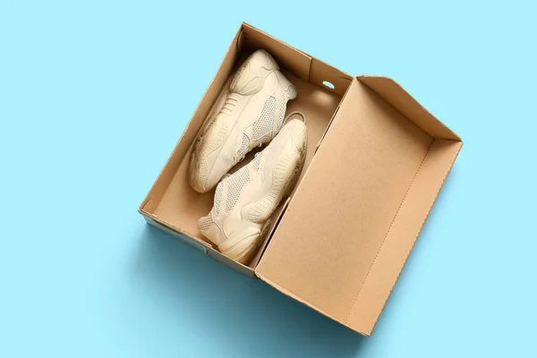 Cardboard box with sports shoes on light blue background