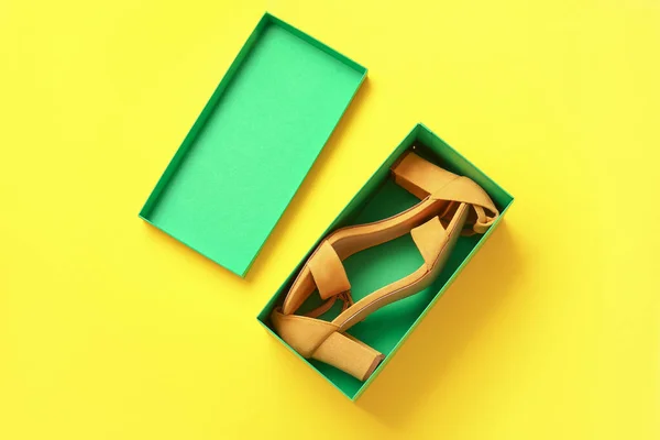 Cardboard box with high heeled sandals on yellow background